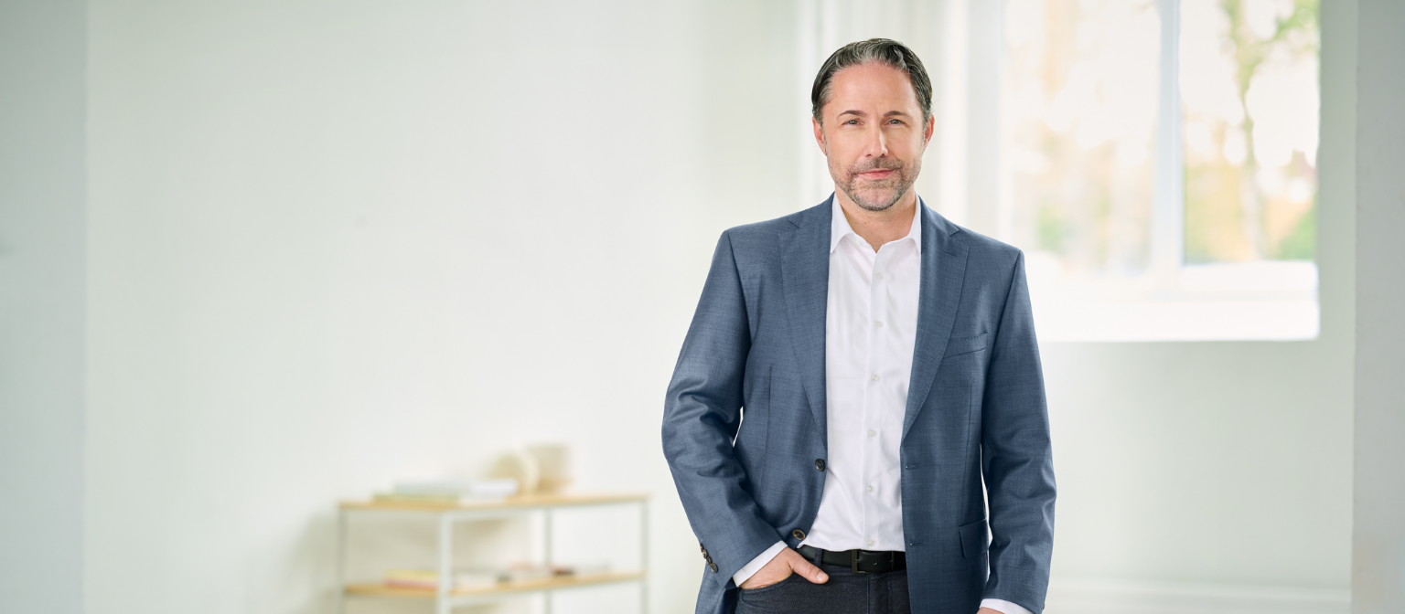 Marwin Ramcke, CEO, dans une pièce lumineuse, vêtu d’un costume bleu, la main droite dans la poche de son pantalon. 