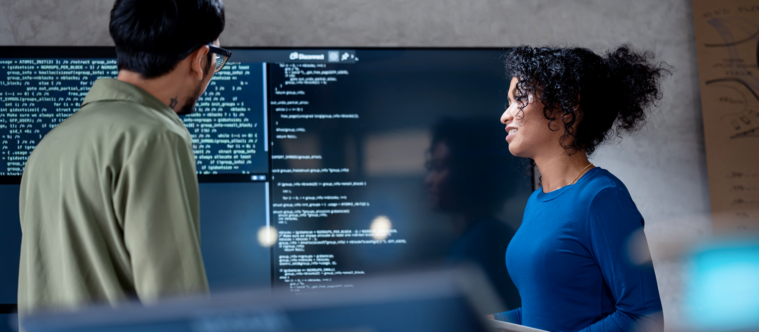 IA dans le recouvrement de créances : sur cette image, deux professionnels analysent collaborativement du code de programme pour des processus automatisés sur un grand écran. La scène illustre l'application pratique de l'intelligence artificielle (IA) et de l'automatisation des processus robotiques (RPA) dans la gestion des créances – un exemple de transformation numérique dans la gestion des créances.