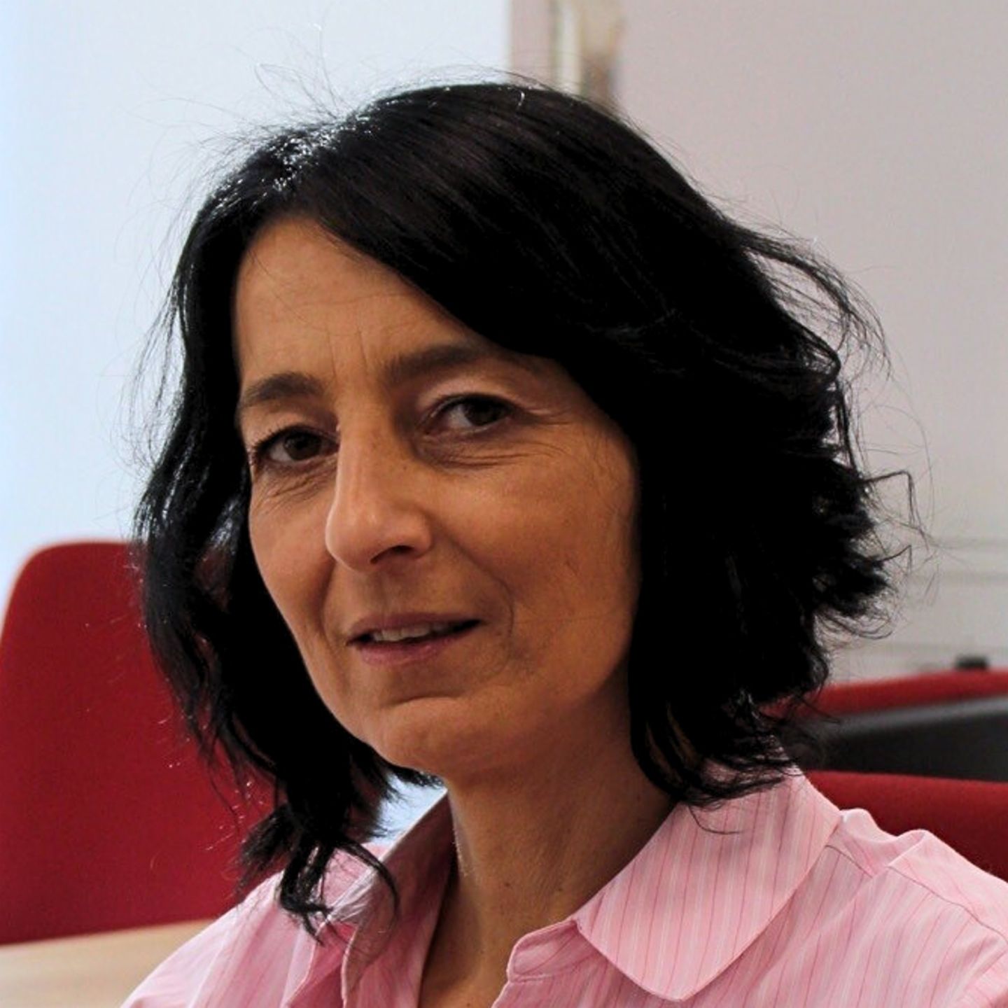 Cristina Pasere, Responsable du Support Opérationnel de Conformité chez EOS Roumanie. Cristina Pasere, Responsable du Support Opérationnel de Conformité chez EOS Roumanie, est assise à son bureau, vêtue d'un chemisier rayé rose, et regarde la caméra.