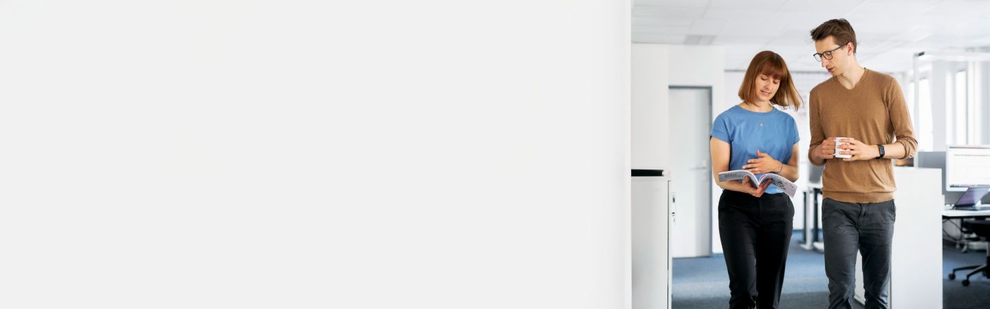 Section Stage Client FAQ Deux collègues discutent dans un bureau moderne de la manière dont EOS peut protéger les entreprises contre les défauts de paiement et maximiser leur liquidité dans la gestion des créances, tandis qu'un autre employé travaille sur l'ordinateur en arrière-plan.