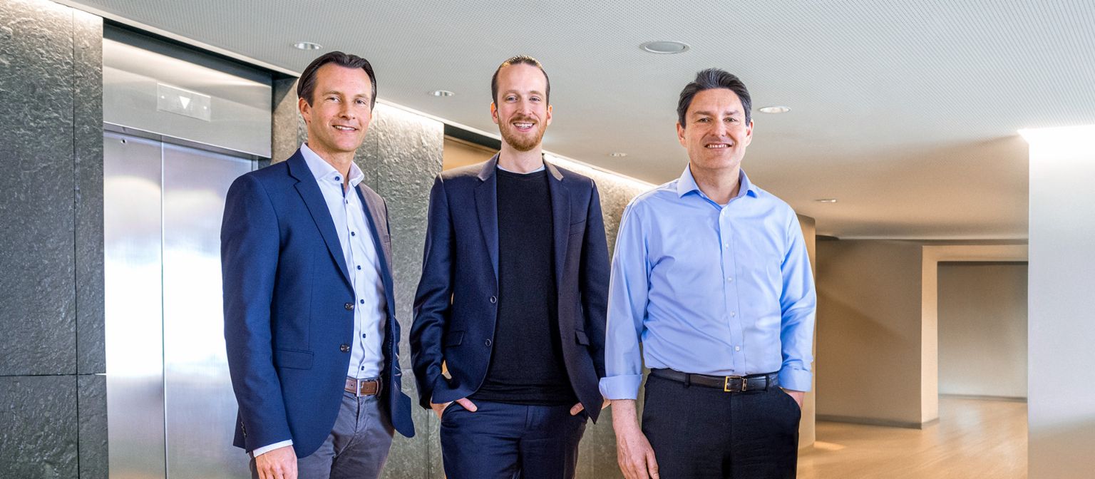 Trois membres masculins du conseil d'administration du Groupe EOS se tiennent en tenue professionnelle devant des ascenseurs dans un cadre moderne.